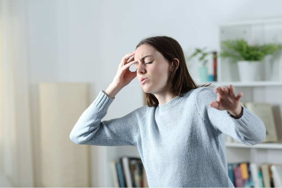 Woman touching her forehead and reaching for balance while feeling dizzy at home.