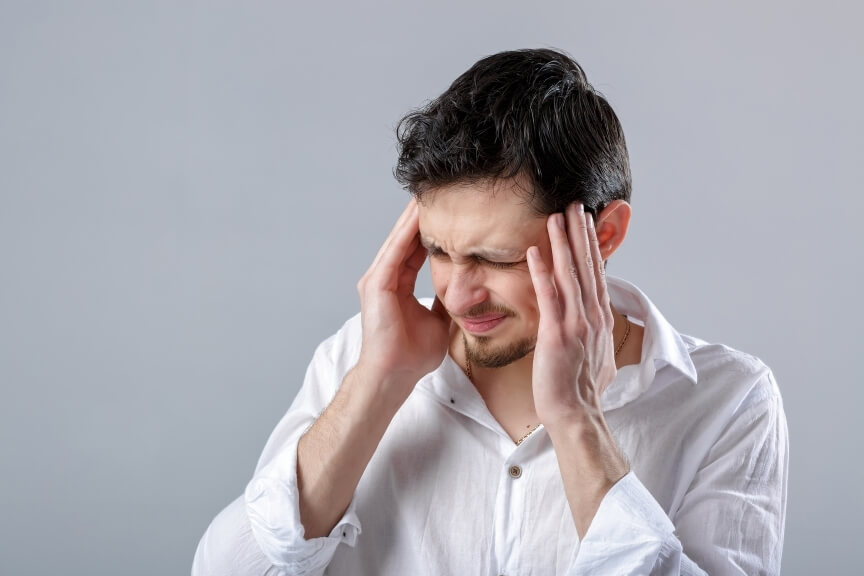 Man holding both sides of his head with his eyes closed while experiencing migraine pain sensitivity.