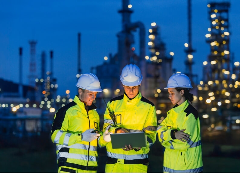 Three workers in high-visibility clothing on an industrial night shift, representing the challenges of shift work and migraines.