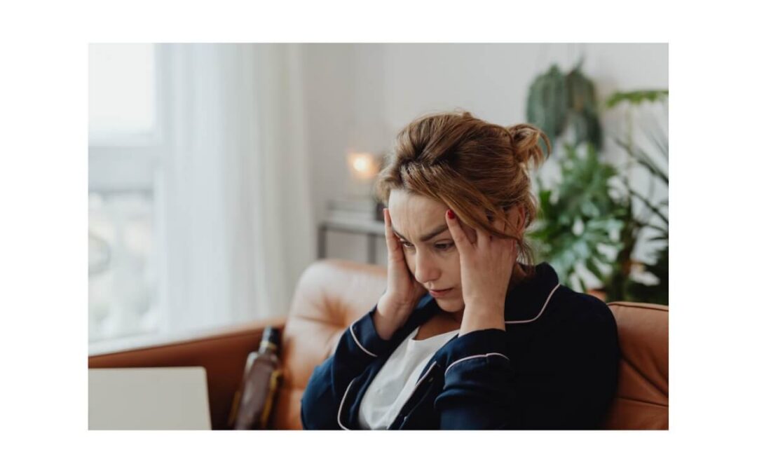 A woman sitting indoors with her hands on her head, showing the frustration of headache symptoms after a busy day.