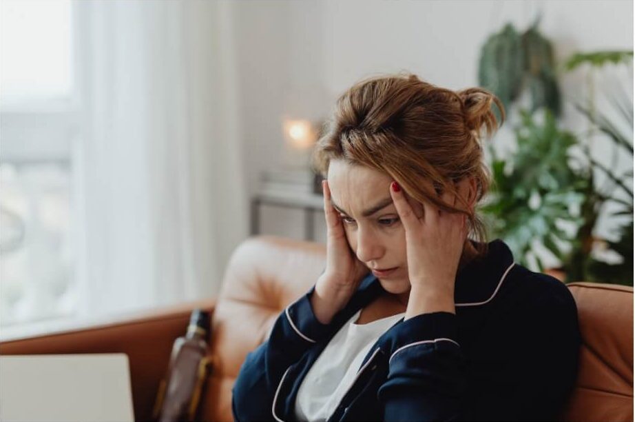 A woman sitting indoors with her hands on her head, showing the frustration of headache symptoms after a busy day.