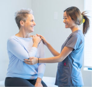 A physiotherapist assisting a smiling patient with shoulder mobility during a clinical session—supporting recovery from cervicogenic dizziness.