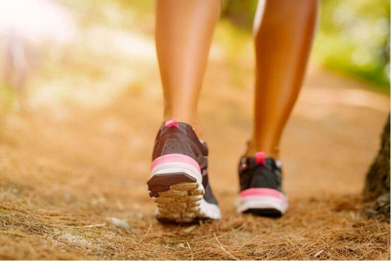 Person walking along a leafy forest trail, symbolising the role of gentle exercise in achieving headache relief through walking.