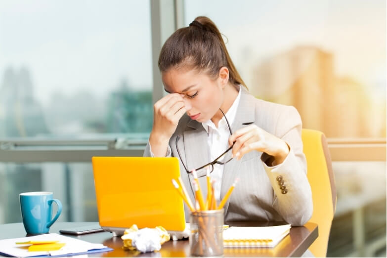 Office worker holding her head at a desk experiencing stress headaches during work