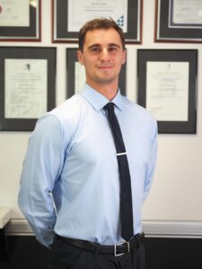 Portrait of Headache clinician Matt Ivan in clinic setting with certificates, representing his expertise in treating migraines and headaches at Gold Coast Headache and Migraine Clinic.